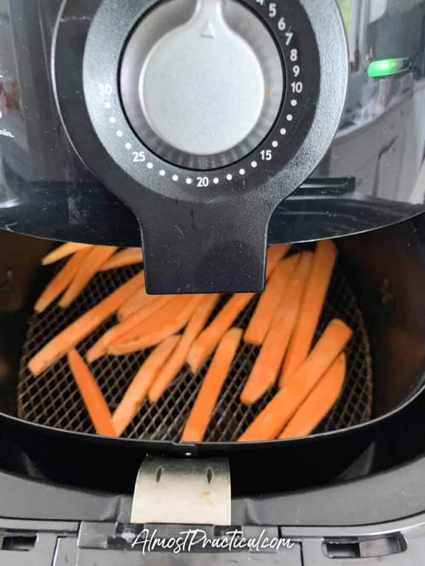 Air fryer with basket half open showing how sweet potato fries inside should be spaced for even cooking.