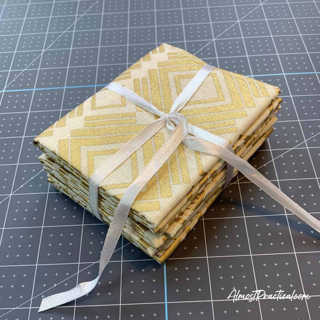 fat quarter stack of fabric in cream and gold tied with a white ribbon