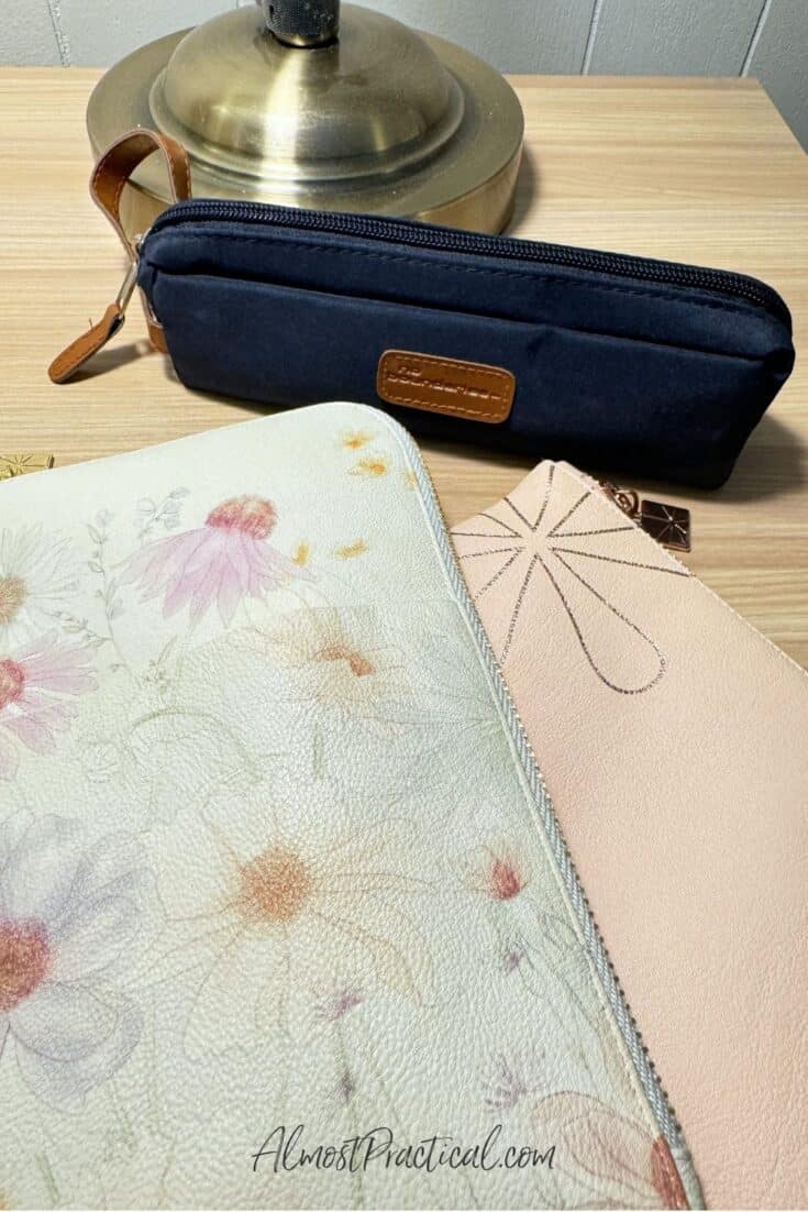 Three pencil pouches. One with a floral pattern, one is pink, and a dark blue one.